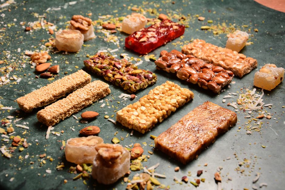 Barres de céréales maison variées disposées sur un fond vert, entourées de fruits secs et de noix.