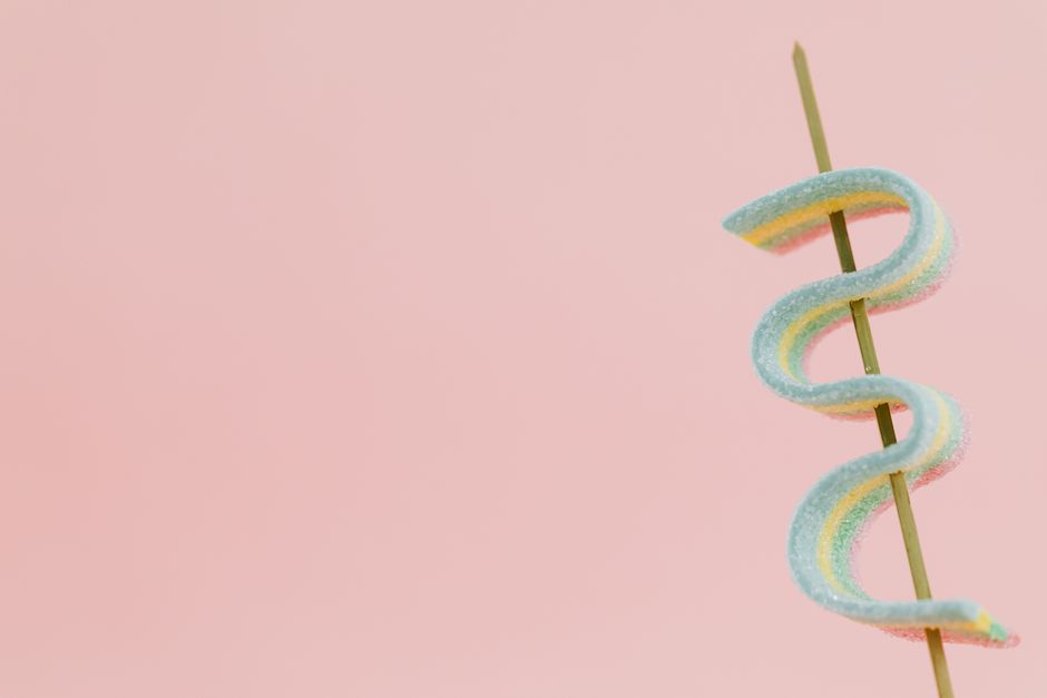 Brochette en bois avec une guimauve colorée en forme de serpent sur fond rose.