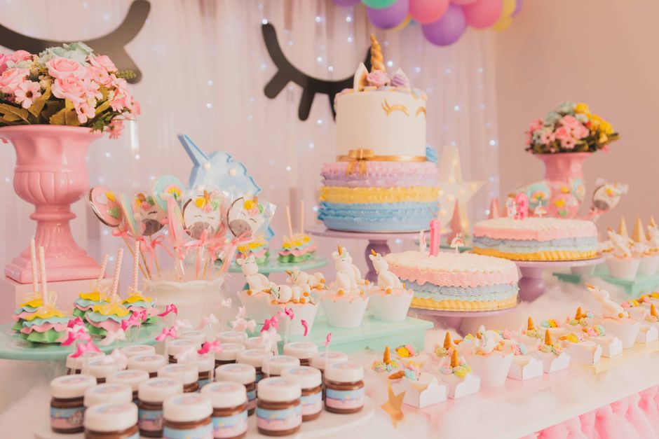 Table décorée pour un anniversaire avec plusieurs gâteaux colorés, bonbons et fleurs, ambiance festive et joyeuse.