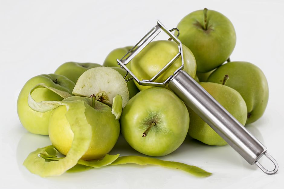 Pommes vertes avec un éplucheur en métal et des épluchures sur une surface blanche.
