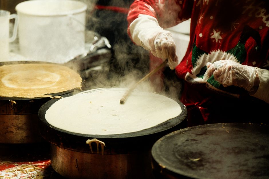 Préparation de crêpes légères sur une crêpière, avec de la vapeur s'échappant et une main tenant une spatule.