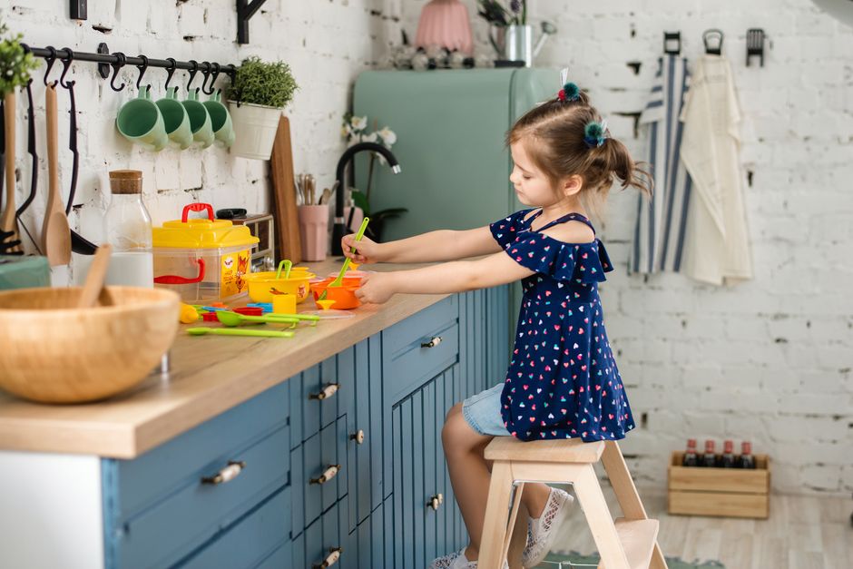Une petite fille prépare des collations colorées dans une cuisine moderne, assise sur un tabouret en bois.