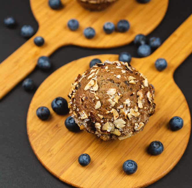 Muffins aux myrtilles garnis d'avoine, posés sur des planches en bois, entourés de myrtilles fraîches.