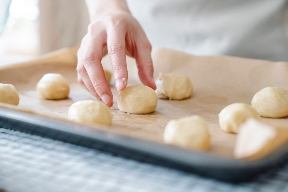 Main formant des boules de pâte sur une plaque recouverte de papier sulfurisé pour un goûter adapté aux allergies.