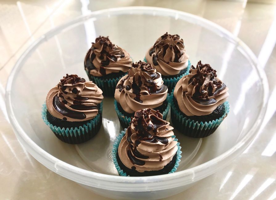 Six cupcakes au chocolat avec un topping vanille, décorés de vermicelles en chocolat dans un plat transparent.