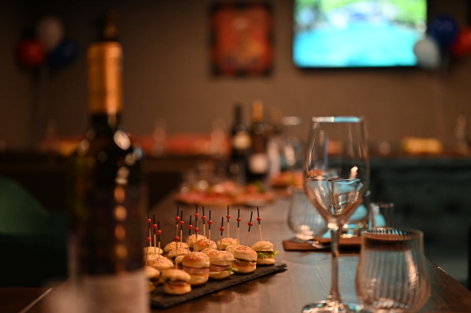 Mini-burgers briochés garnis de jambon et fromage, présentés sur une table avec des verres et des bouteilles de vin.
