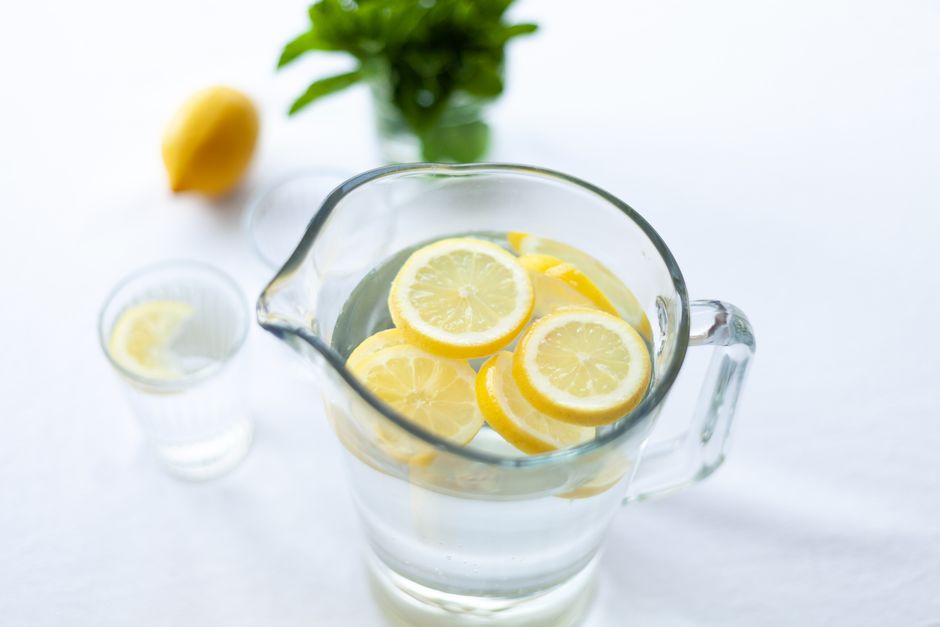 Pichet de citronnade avec des rondelles de citron, verre à côté et menthe en arrière-plan.