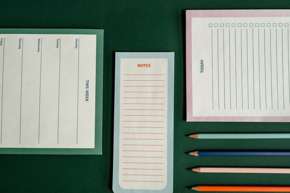 Papier à lettres et crayons disposés sur une table verte, idéal pour rédiger une liste de courses pour un goûter.