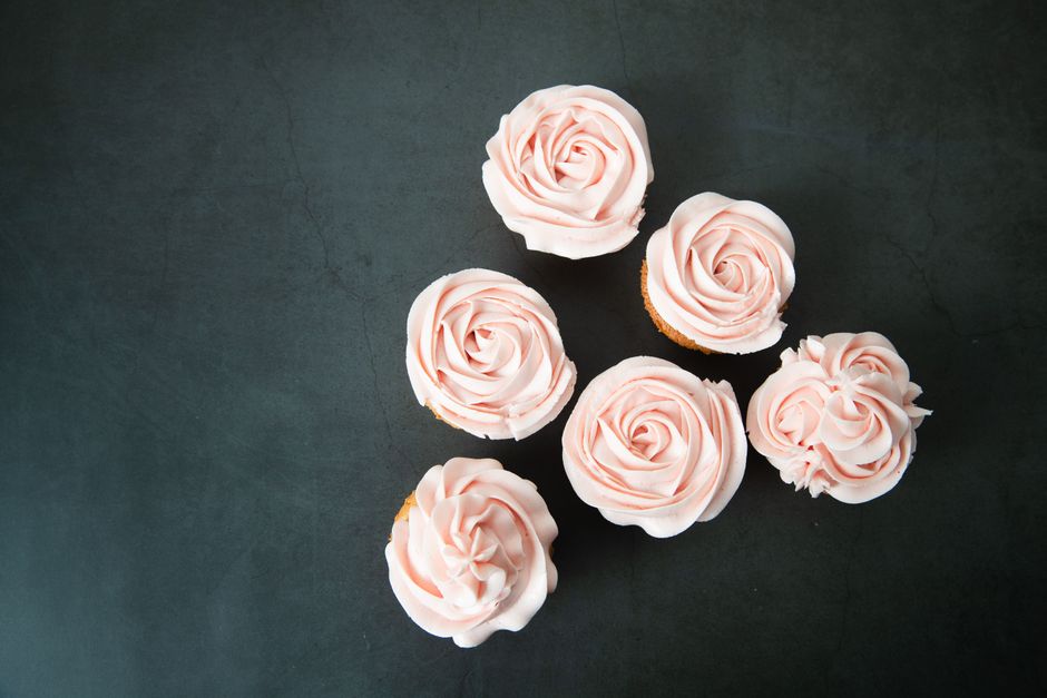 Six cupcakes décorés de crème rose en forme de rose sur un fond sombre.