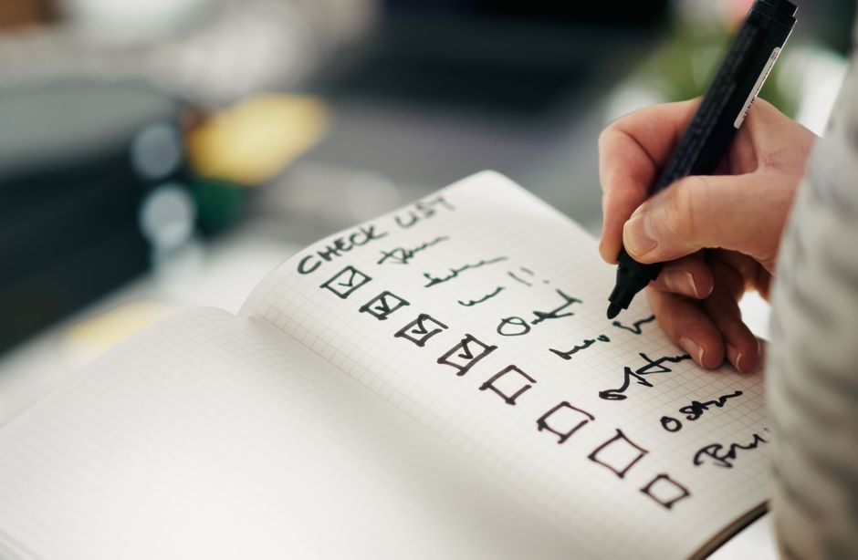 Main tenant un carnet avec une liste de courses pour un goûter, des cases cochées et des éléments écrits.