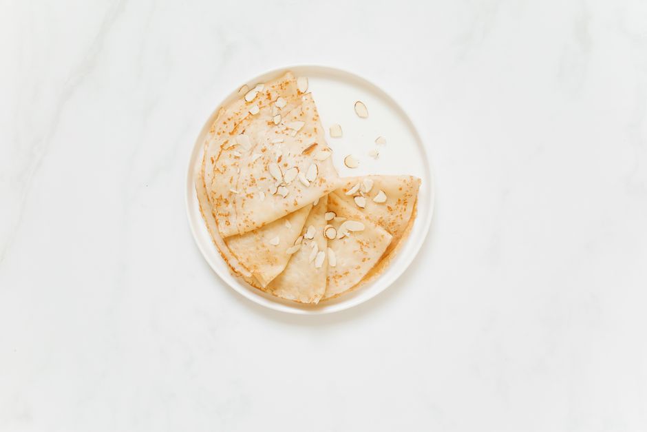 Assiette de crêpes légères garnies d'amandes effilées sur fond blanc.