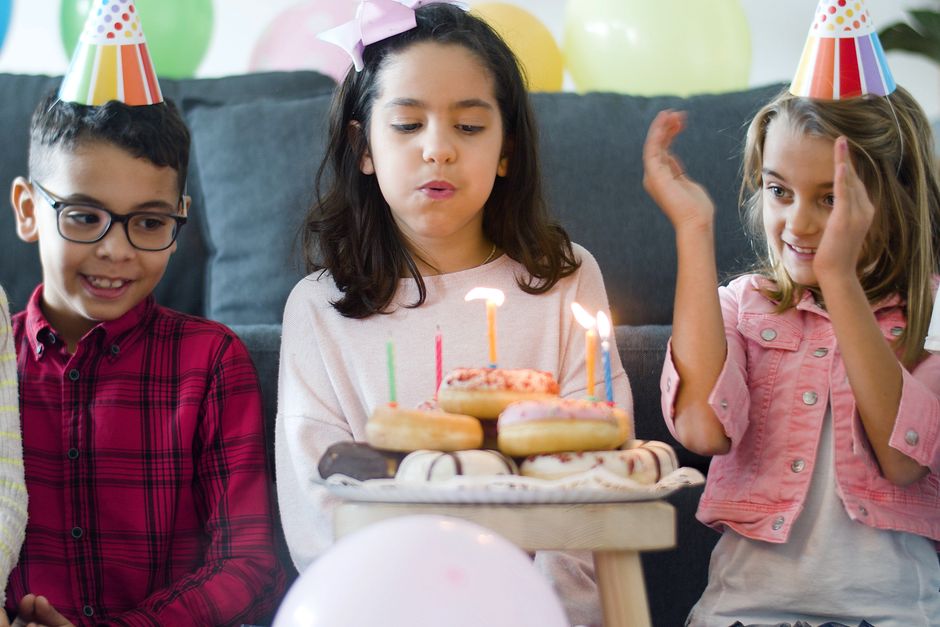 Enfants célébrant un anniversaire autour d'un gâteau avec des bougies et des donuts, décorations festives en arrière-plan.