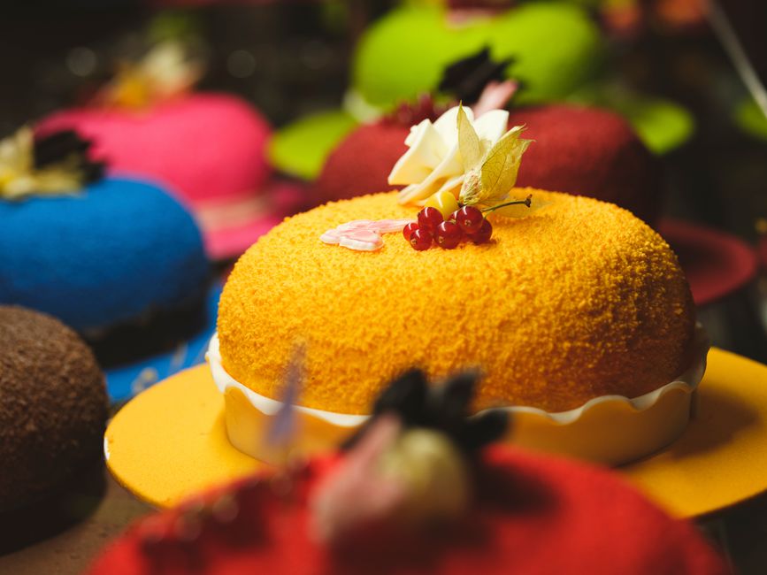 Gâteau d'anniversaire coloré avec décoration florale et fruits sur un fond de plusieurs gâteaux variés.