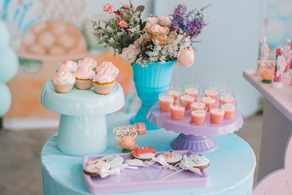Table de goûter colorée avec cupcakes, desserts en verrines et biscuits décorés, entourée de fleurs.
