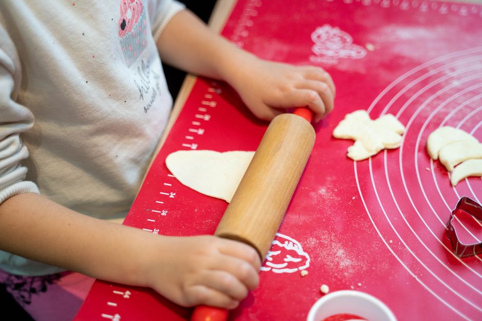 Enfant utilisant un rouleau à pâtisserie pour étaler de la pâte sur un plan de travail, avec des emporte-pièces à proximité.