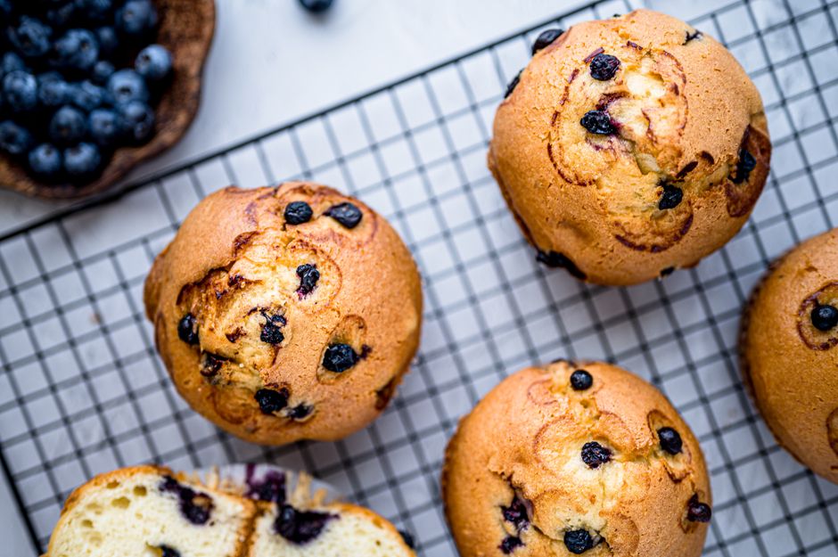 Muffins aux myrtilles dorés sur une grille, avec des myrtilles fraîches en arrière-plan.
