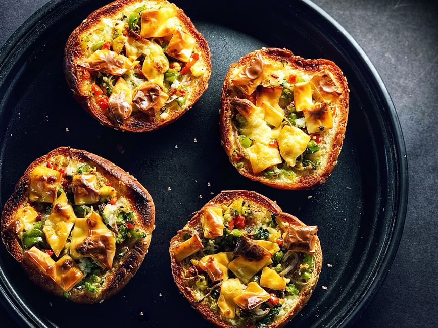 Mini-pizzas sucrées garnies de fruits et chocolat sur un plat noir, prêtes à être dégustées.