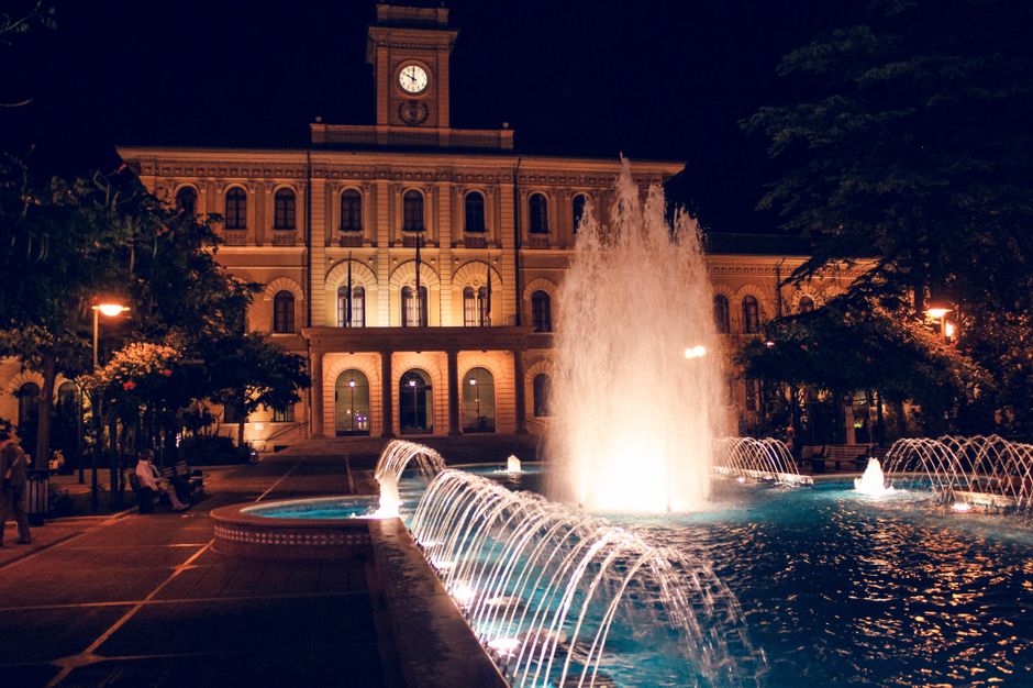 Fontaine illuminée devant un bâtiment historique la nuit, créant une ambiance paisible et relaxante.