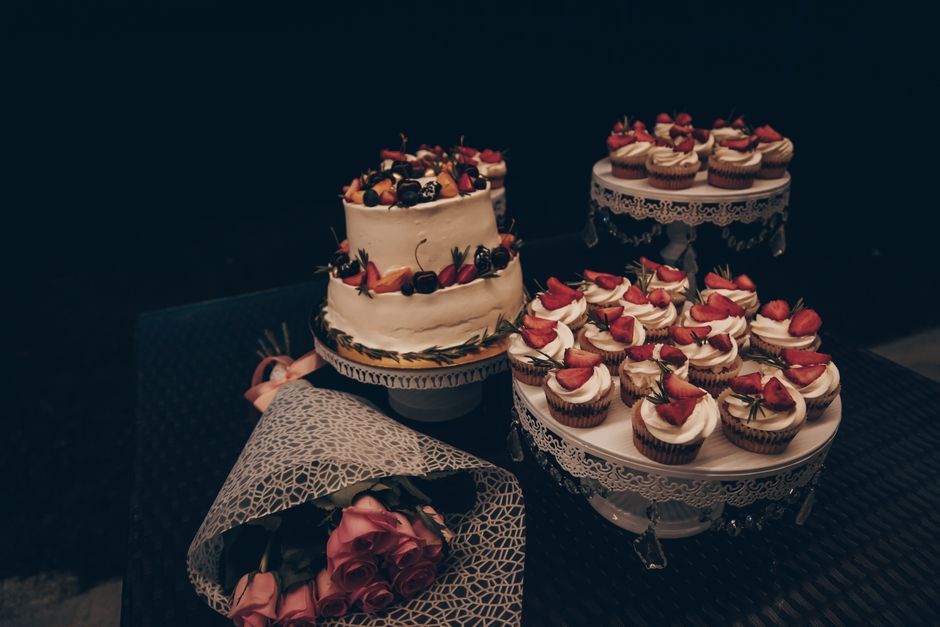 Table de goûter avec un gâteau décoré de fruits et des cupcakes garnis de fraises, accompagnés d'un bouquet de roses.
