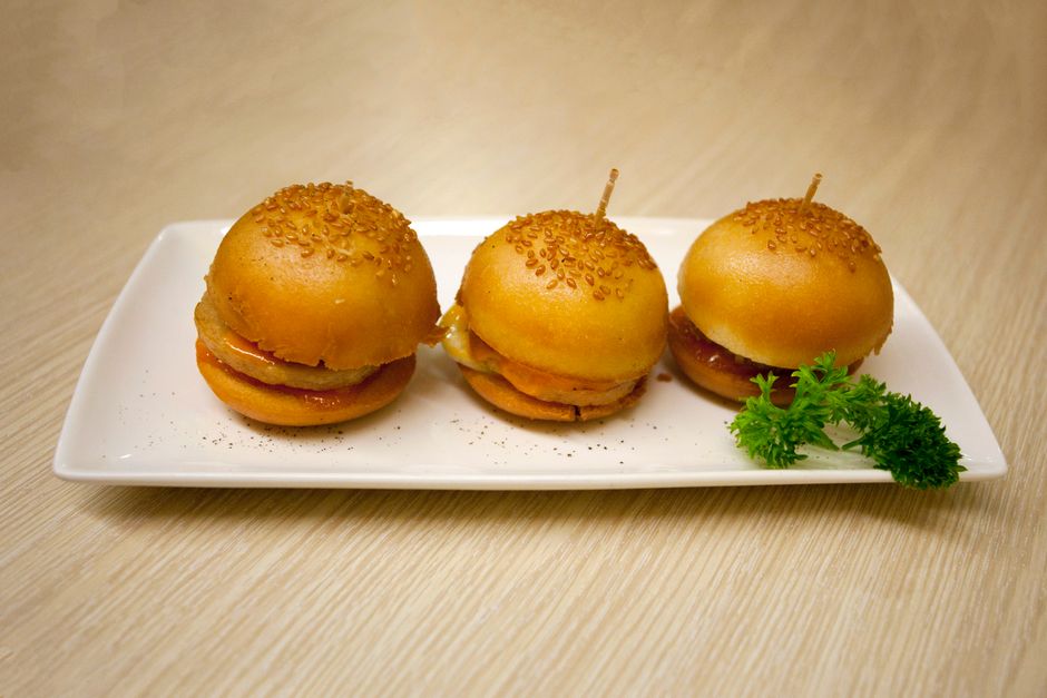Mini-burgers briochés garnis de jambon et fromage, présentés sur une assiette avec une touche de persil.