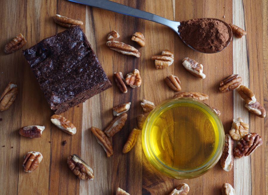 Brownie fondant au chocolat entouré de noix de pécan et d'une cuillère de cacao sur une planche en bois.