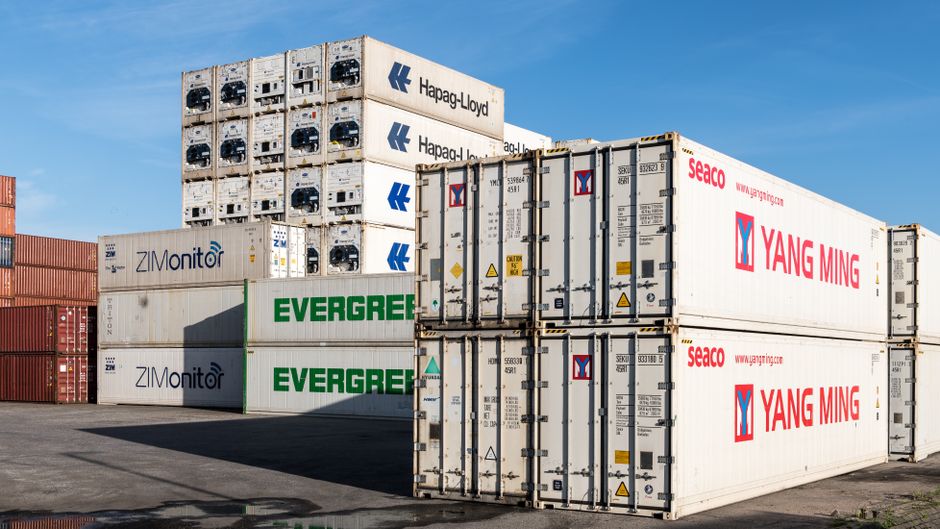 Conteneurs de transport empilés dans un port, avec un ciel bleu en arrière-plan.