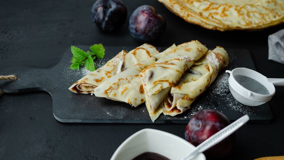 Crêpes légères garnies de confiture, servies sur une planche avec des prunes et de la menthe.