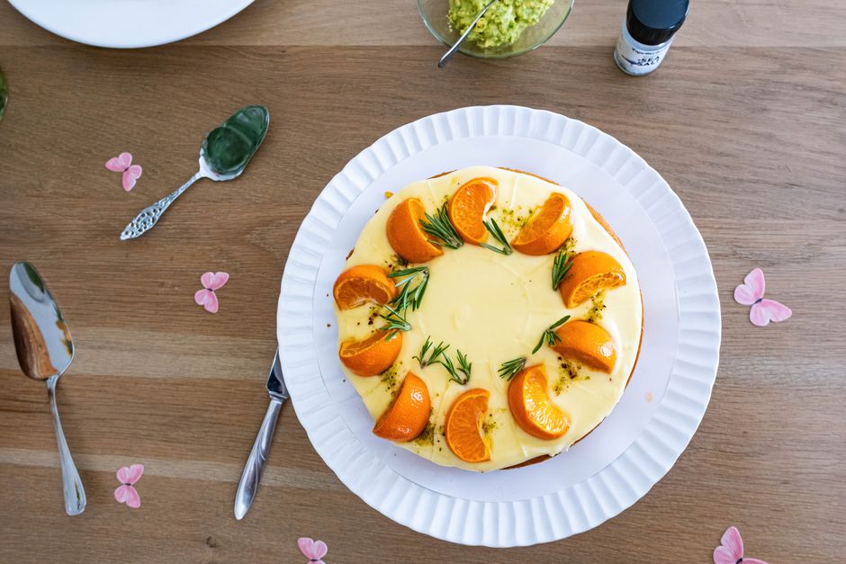 Gâteau au yaourt décoré d'orange et de romarin sur une assiette blanche, posé sur une table en bois.