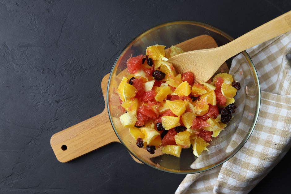 Salade de fruits colorée dans un bol en verre avec morceaux d'orange, pamplemousse et raisins secs, accompagnée d'une cuillèr