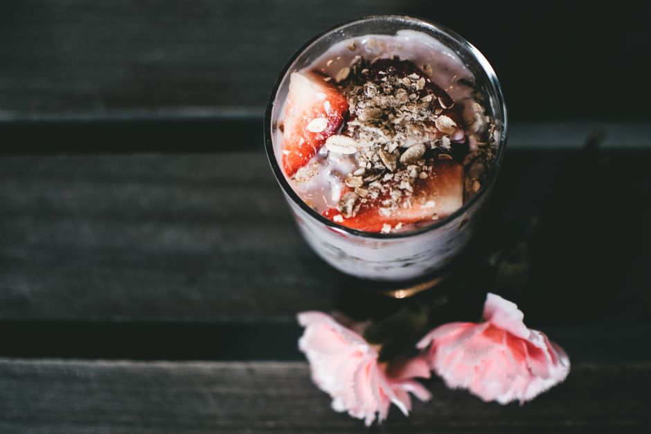 Verrine de fromage blanc garnie de miel, fruits rouges et graines, posée sur une table en bois avec des fleurs.