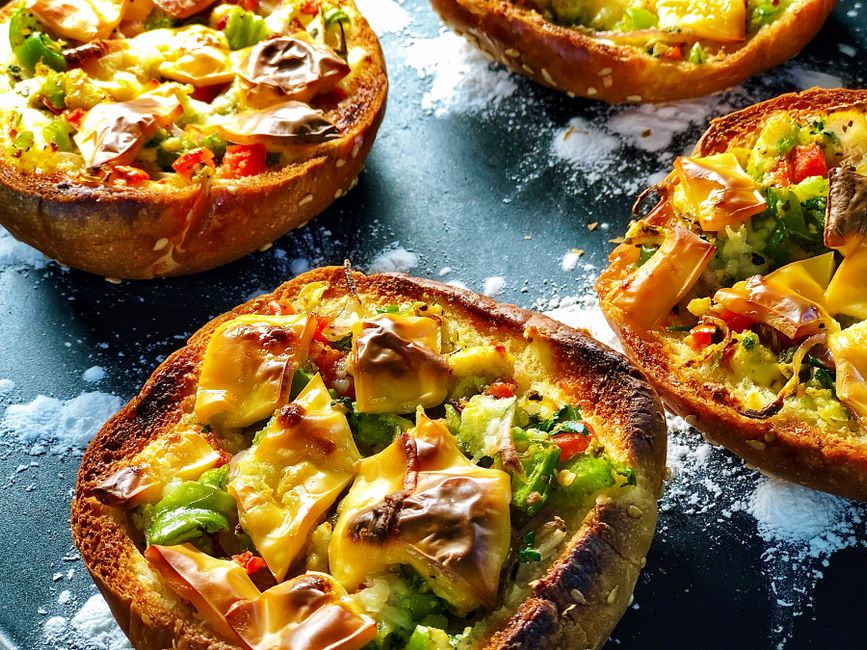 Mini-pizzas sucrées garnies de légumes colorés et de fromage, présentées sur un plateau noir.