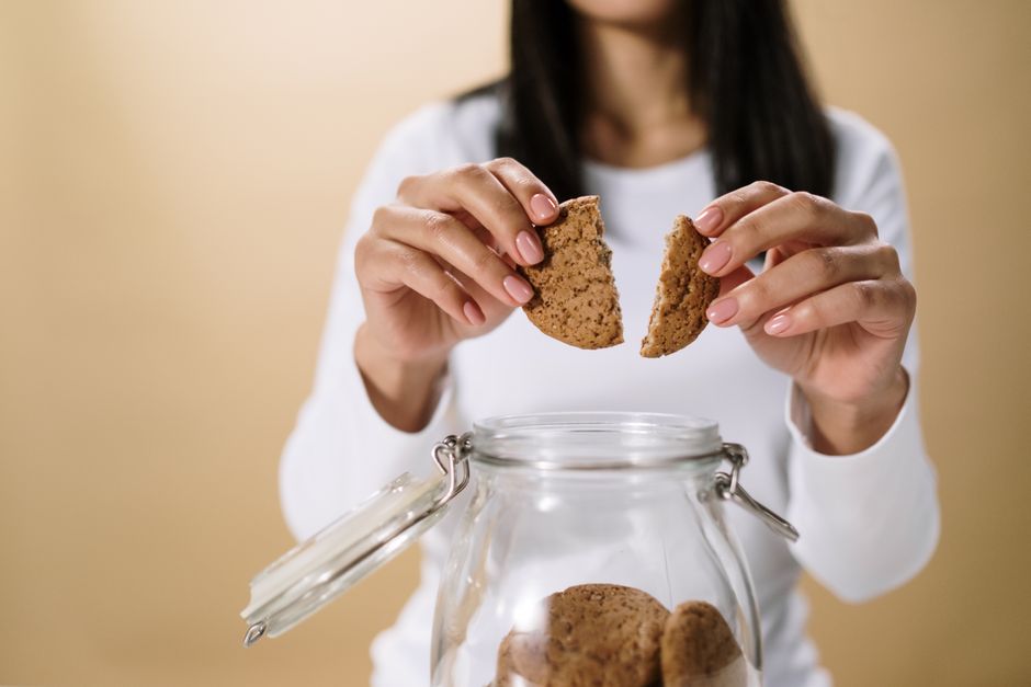 Femme tenant un biscuit en deux au-dessus d'un bocal en verre rempli de biscuits.