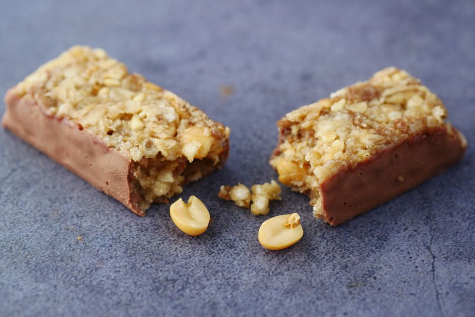 Barres de céréales maison coupées en deux, garnies de flocons d'avoine et de chocolat, avec des cacahuètes visibles.