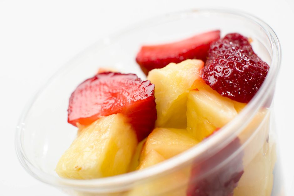 Salade de fruits frais avec morceaux d'ananas, fraises et framboises dans un verre transparent.