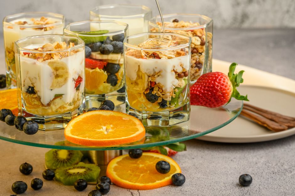 Verrines de fromage blanc garnies de miel, fruits rouges et granola, présentées sur un plateau en verre.