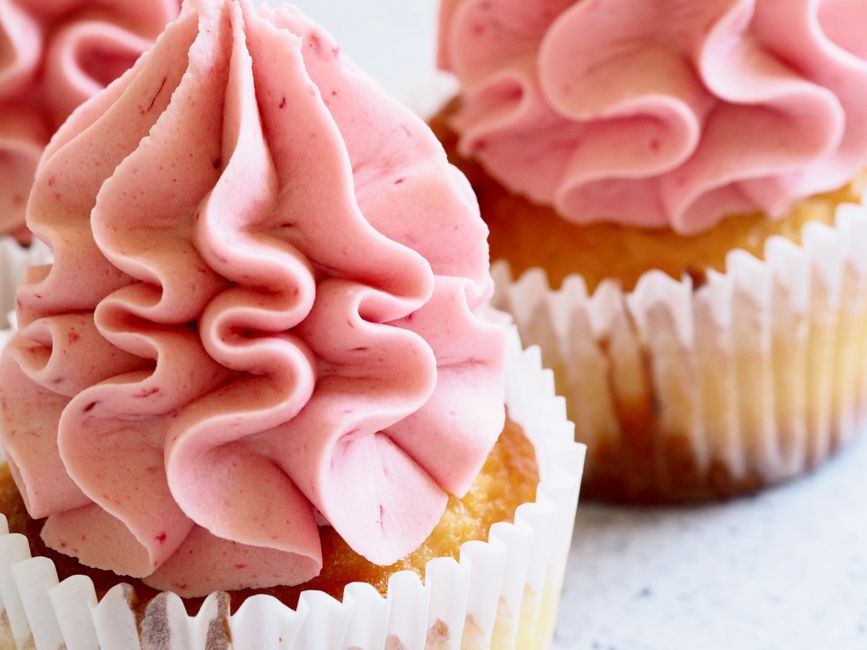 Deux cupcakes avec un topping en crème rose en forme de volutes, présentés sur un fond clair.