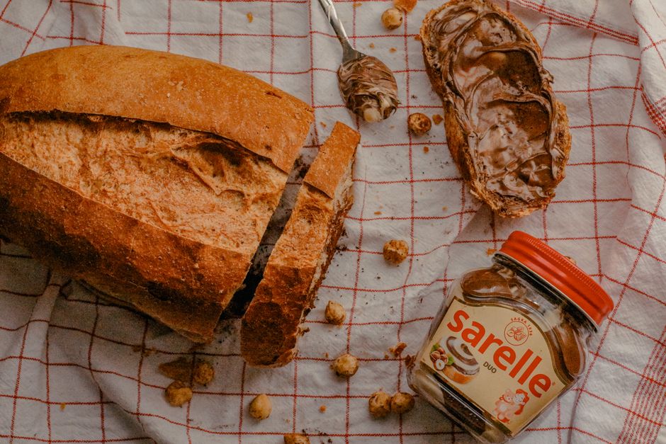 Pain tranché avec de la pâte à tartiner noisette et un pot de pâte à tartiner sur un torchon à carreaux.